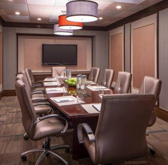 Hotel meeting room, featuring long wooden table and surrounding leather chairs.