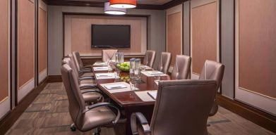 Hotel meeting room, featuring long wooden table and surrounding leather chairs.