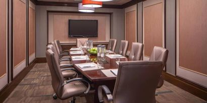 Hotel meeting room, featuring long wooden table and surrounding leather chairs.