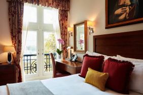 Double door view of outside with wooden desk workspace alongside guest queen bed.