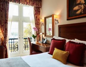 Double door view of outside with wooden desk workspace alongside guest queen bed.