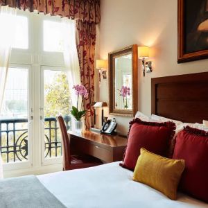 Double door view of outside with wooden desk workspace alongside guest queen bed.