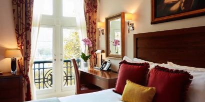 Double door view of outside with wooden desk workspace alongside guest queen bed.