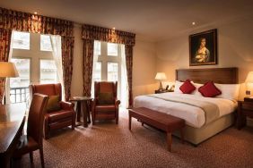 Deluxe king room at The Royal Horseguards Hotel, featuring numerous leather chairs, large windows, and a desk.