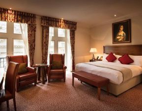 Deluxe king room at The Royal Horseguards Hotel, featuring numerous leather chairs, large windows, and a desk.