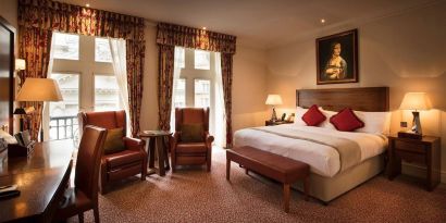 Deluxe king room at The Royal Horseguards Hotel, featuring numerous leather chairs, large windows, and a desk.