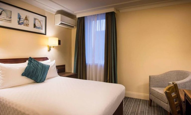 Double bed in a standard room at the Thistle London Heathrow Terminal 5, with nearby window and chair.