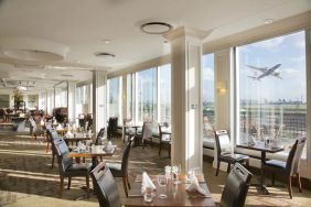 Sunlight room with floor to ceiling windows spanning the entire length of the wall to see planes takeoff and land at London Heathrow Airport.