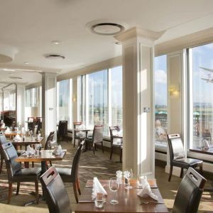 Sunlight room with floor to ceiling windows spanning the entire length of the wall to see planes takeoff and land at London Heathrow Airport.