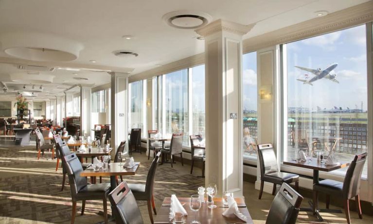 Sunlight room with floor to ceiling windows spanning the entire length of the wall to see planes takeoff and land at London Heathrow Airport.