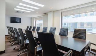 Hotel meeting room with long table, large windows and TV, and seating for over a dozen attendees.