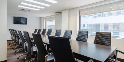 Hotel meeting room with long table, large windows and TV, and seating for over a dozen attendees.