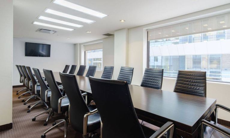 Hotel meeting room with long table, large windows and TV, and seating for over a dozen attendees.