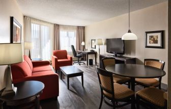 Guest room lounge in Les Suites Hotel Ottawa, with workspace desk and chair, plus sofa, chairs, and tables.