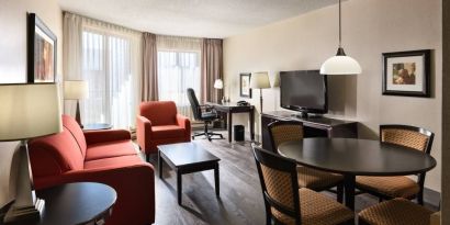 Guest room lounge in Les Suites Hotel Ottawa, with workspace desk and chair, plus sofa, chairs, and tables.