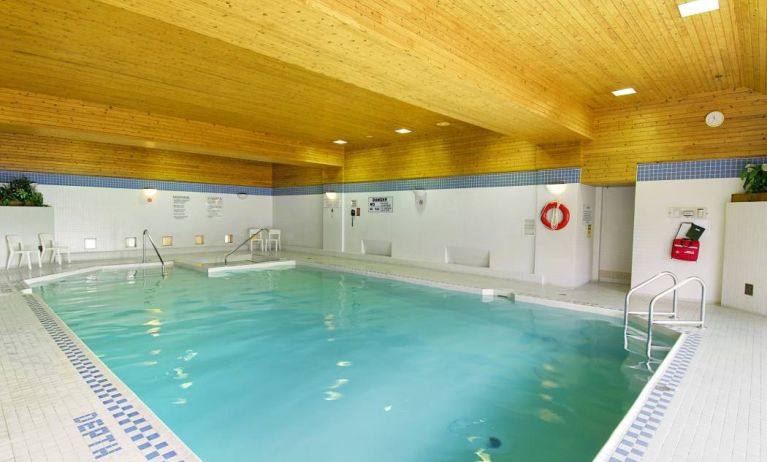 The hotel’s indoor pool is brightly lit and has chairs by the side.