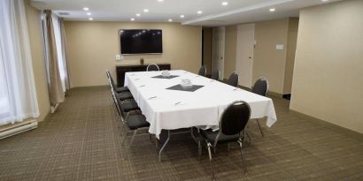 Meeting room in Les Suites Hotel Ottawa, with long table, ten chairs around it, and a large television.