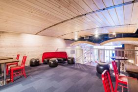 Second floor loft with arc planked ceiling, blue carpet, red chairs and small tables to work or socialize from.