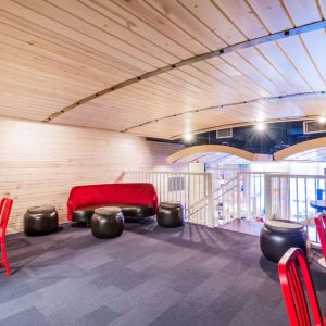 Second floor loft with arc planked ceiling, blue carpet, red chairs and small tables to work or socialize from.