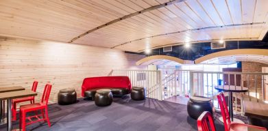 Second floor loft with arc planked ceiling, blue carpet, red chairs and small tables to work or socialize from.