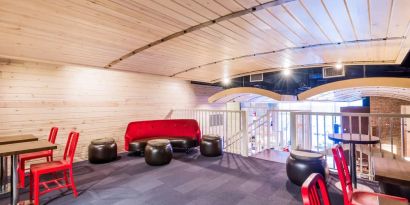 Second floor loft with arc planked ceiling, blue carpet, red chairs and small tables to work or socialize from.