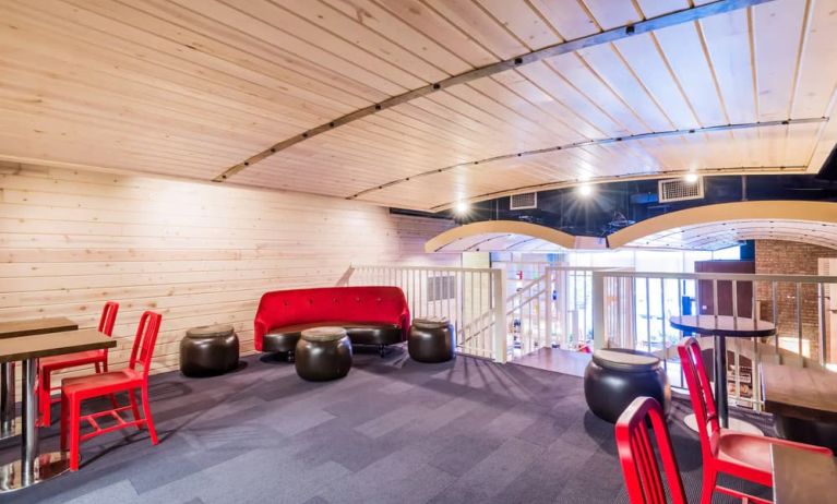 Second floor loft with arc planked ceiling, blue carpet, red chairs and small tables to work or socialize from.