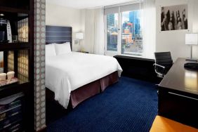 Guest room of the Hilton Fashion District, complete with king-sized bed and workspace desk and chair.