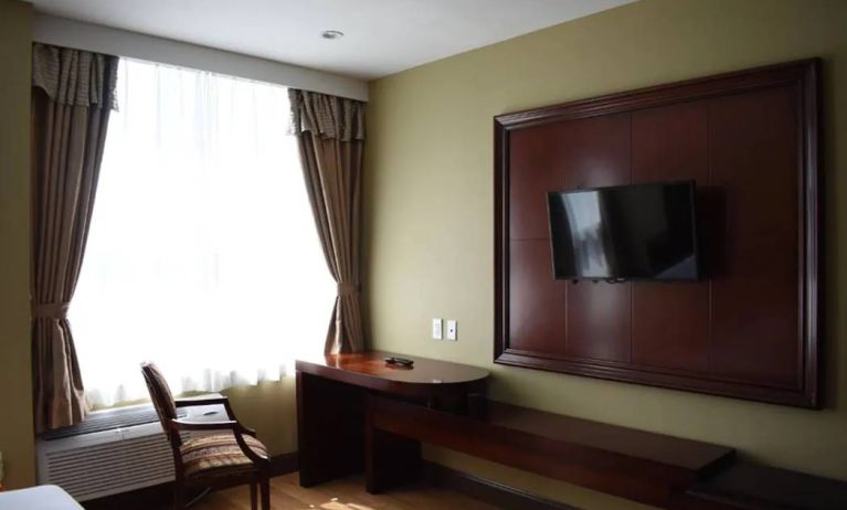 A Queens Hotel guest room with chair and table for working, and a nearby window.