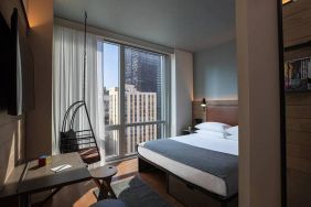 Moxy NYC Downtown double bed guest room, with large television, floor-to-ceiling window, and desk for working.