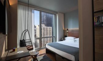 Moxy NYC Downtown double bed guest room, with large television, floor-to-ceiling window, and desk for working.