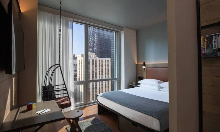 Moxy NYC Downtown double bed guest room, with large television, floor-to-ceiling window, and desk for working.