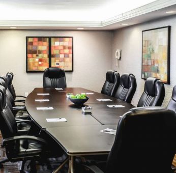 A meeting room with long wooden table and ten leather chairs around it.