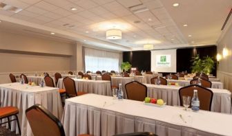 Meeting room with numerous tables and seating arranged to face a lectern, beside which is a projector screen.