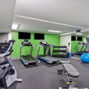 The hotel fitness center has racks of weights, large TV screens, and assorted exercise machines.