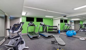 The hotel fitness center has racks of weights, large TV screens, and assorted exercise machines.