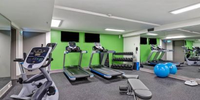 The hotel fitness center has racks of weights, large TV screens, and assorted exercise machines.