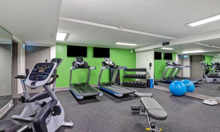 The hotel fitness center has racks of weights, large TV screens, and assorted exercise machines.