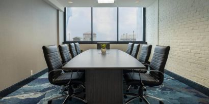 Hotel meeting room with a long wooden table and surrounding leather chairs.