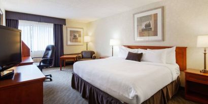 Guest room in Best Western North Bay, with large double bed, window, and armchair.