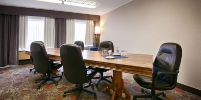 Hotel meeting with long wooden table and quintet of leather chairs around it.