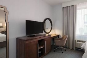 Wooden dark-stained television stand with TV, workspace to the right with desk lamp, phone, mirror directly ahead.