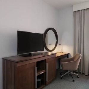 Wooden dark-stained television stand with TV, workspace to the right with desk lamp, phone, mirror directly ahead.