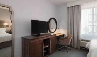 Wooden dark-stained television stand with TV, workspace to the right with desk lamp, phone, mirror directly ahead.