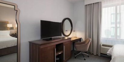 Wooden dark-stained television stand with TV, workspace to the right with desk lamp, phone, mirror directly ahead.