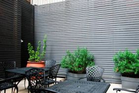 Patio with tall black privacy fences and black wrought iron tables and chairs for four people, at the Hampton Inn Manhattan - Madison Square Garden.