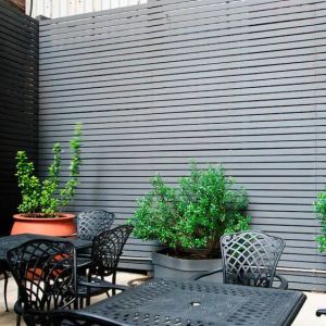 Patio with tall black privacy fences and black wrought iron tables and chairs for four people, at the Hampton Inn Manhattan - Madison Square Garden.