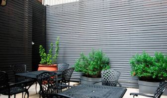 Patio with tall black privacy fences and black wrought iron tables and chairs for four people, at the Hampton Inn Manhattan - Madison Square Garden.