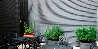 Patio with tall black privacy fences and black wrought iron tables and chairs for four people, at the Hampton Inn Manhattan - Madison Square Garden.