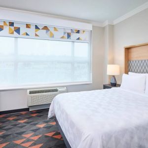 Double bed guest room in Holiday Inn & Suites Oakville At Bronte, with large window and bedside lamp.