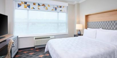 Double bed guest room in Holiday Inn & Suites Oakville At Bronte, with large window and bedside lamp.